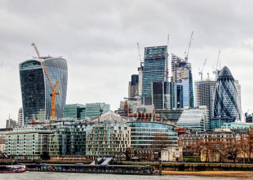 London skyline along the Thames with the Walkie Talkie building on the left, The Gherkin on the right, and construction cranes overhead under a cloudy sky.