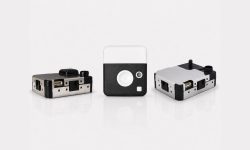 Three small modular electronic devices with metal housings and black panels arranged on a white reflective surface, likely prototype modules or adapters.