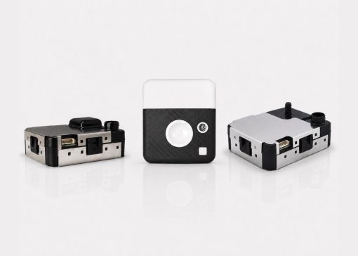 Three small modular electronic devices with metal housings and black panels arranged on a white reflective surface, likely prototype modules or adapters.