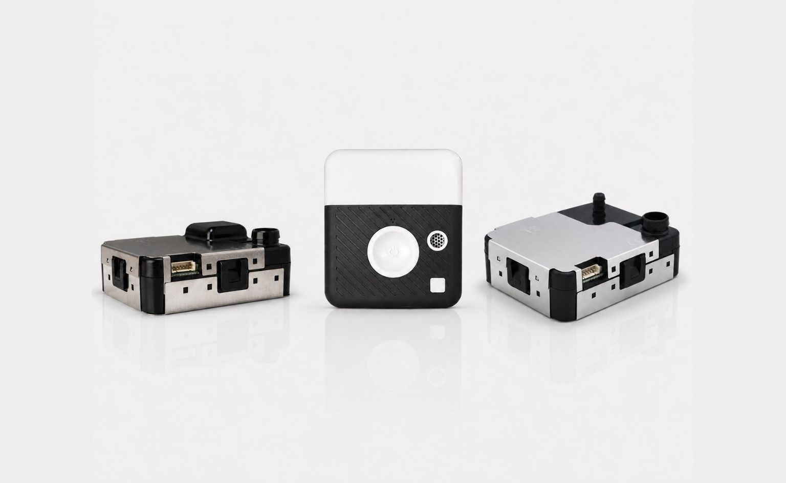 Three small modular electronic devices with metal housings and black panels arranged on a white reflective surface, likely prototype modules or adapters.