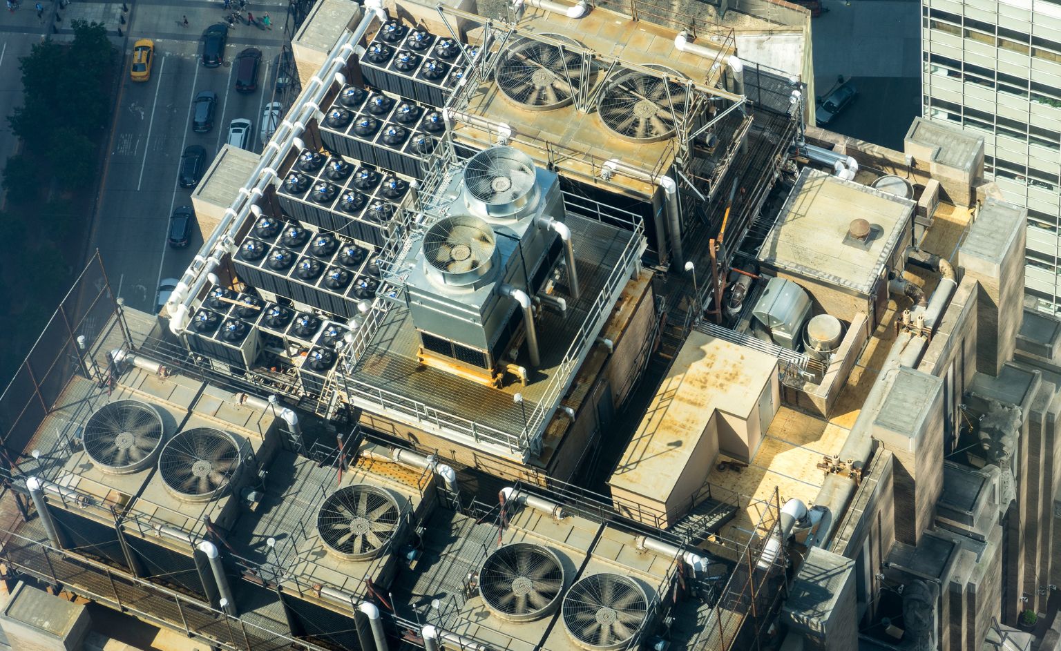 Upholding and promoting the highest levels of air quality and building health with VOC sensors and detection-2 | ION SENSE Aerial view of a building roof with numerous large ventilation fans and machinery arranged in rows under metal walkways.",