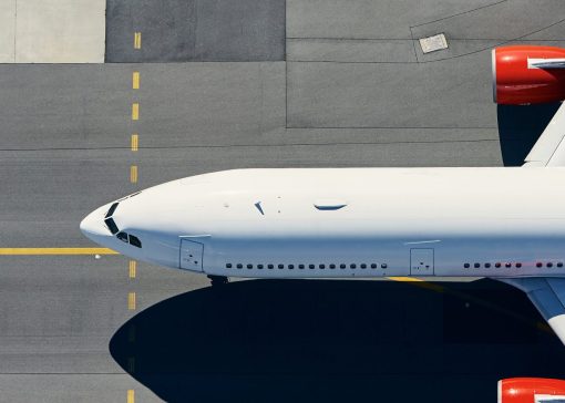 Top-down view of a white commercial airplane parked on gray tarmac with yellow taxiway lines and red engine nacelles.