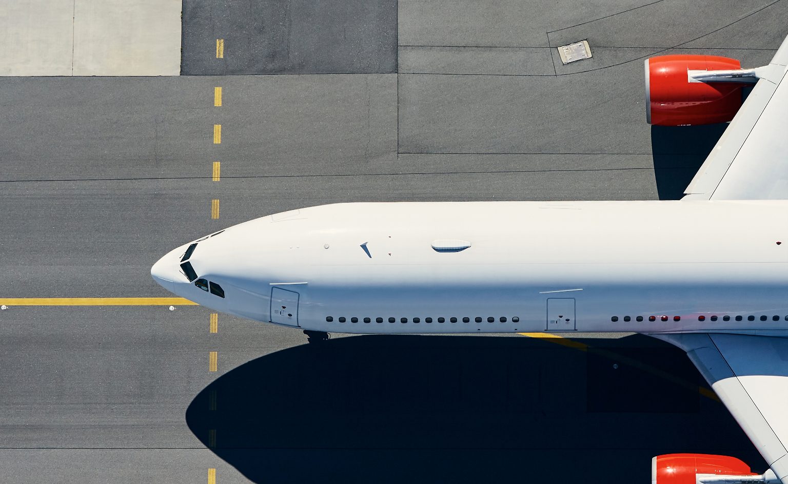 Real-Time VOC Detection at Airports | ION SENSE Top-down view of a white commercial airplane parked on gray tarmac with yellow taxiway lines and red engine nacelles.